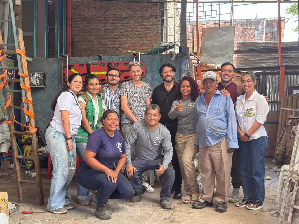 Vista aérea de Cali con un grupo de recicladores y representantes de Swisscontact interactuando frente a un punto de reciclaje marcado con el logo de 'Residuos que Valen ORO'.
