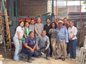 Vista aérea de Cali con un grupo de recicladores y representantes de Swisscontact interactuando frente a un punto de reciclaje marcado con el logo de 'Residuos que Valen ORO'.